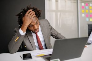 Geschäftsmann sitzt gestresst vor Laptop und hält sich den Kopf als Symbol für Überforderung im Arbeitsalltag