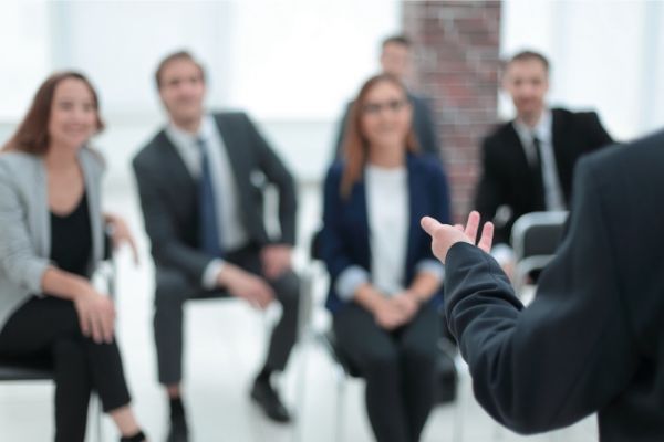 Trainer spricht vor einer Gruppe von Teilnehmenden im Seminar und moderiert eine Diskussion