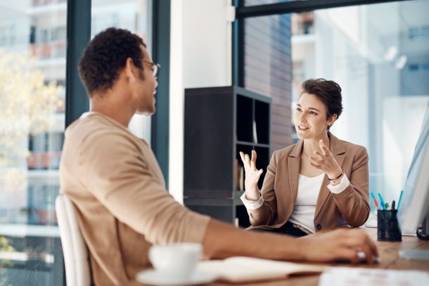 Coach im Gespräch mit Klient im Büro, gestikuliert und erklärt Zusammenhänge