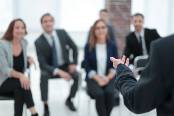 Trainer spricht vor einer Gruppe von Teilnehmenden im Seminar und moderiert eine Diskussion